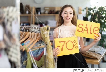 Young woman holding discount sign in clothing store Young woman holding discount sign in clothing store 133012468