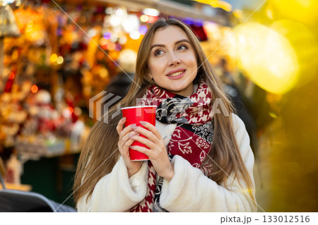 Young woman stands with glass of hot coffee in her hands and enjoys festive New Year atmosphere Young woman stands with glass of hot coffee in her hands and enjoys festive New Year atmosphere 133012516