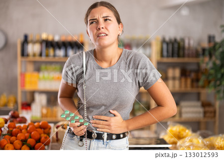 Young woman suffers from abdominal pain, feels pain in her stomach, while visiting grocery supermarket 133012593