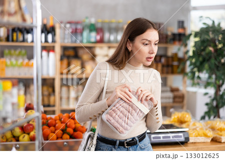 Girl looking at raw bbg sausage in store 133012625