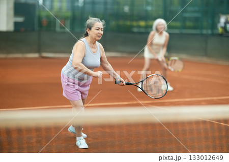 Elderly woman engrossed in doubles tennis game on clay court Elderly woman engrossed in doubles tennis game on clay court 133012649