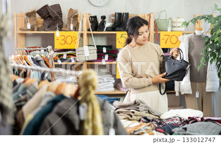 Latin girl is busy looking at clothes items in store, she chooses handbag Latin girl is busy looking at clothes items in store, she chooses handbag 133012747