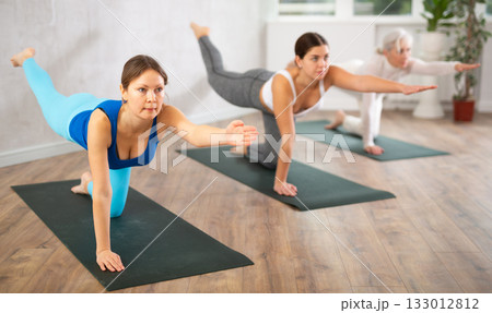 Women of different ages performing Balancing Table restorative Pose or Dandayamana Bharmanasana during yoga training together in studio Women of different ages performing Balancing Table restorative Pose or Dandayamana Bharmanasana during yoga training together in studio 133012812