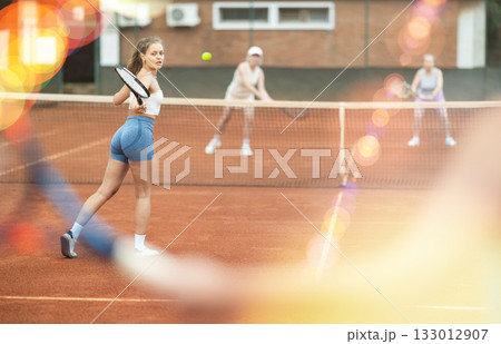 Young female tennis player engrossed in doubles on clay court Young female tennis player engrossed in doubles on clay court 133012907