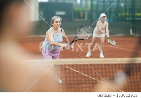 Elderly woman engrossed in doubles tennis game on clay court 133012915