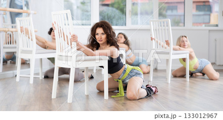Brunette kneeling provocatively before chair during erotic dance at group class Brunette kneeling provocatively before chair during erotic dance at group class 133012967