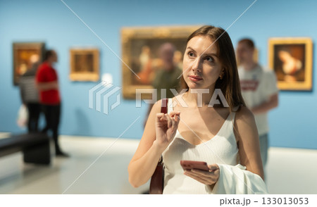 Woman with phone in the hall with paintings 133013053
