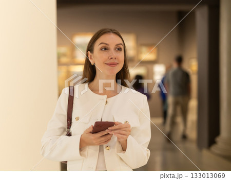While visiting museum, girl uses travel guide application on her phone. 133013069