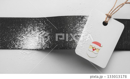 黒い帯の上に雪が散り白いタグにサンタの顔をあしらったクリスマスデザイン　generative ai 133013178