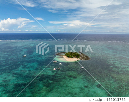 Top view of sandy island with palm trees surrounded by turquoise water and boats nearby. Guyam Island. Siargao, Philippines. 133013783