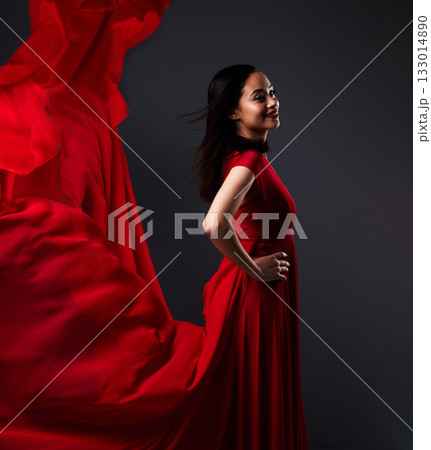 Happy woman, art and fashion, red fabric on dark background with beauty and aesthetic movement. Flowing silk, fantasy and artistic model with smile in creative designer dress in studio with motion. 133014890