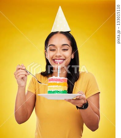 Woman is eating cake, birthday celebration and happy in portrait, rainbow dessert and candle on yellow background. Celebrate, festive and young female, excited for sweet treat and party hat in studio Woman is eating cake, birthday celebration and happy in portrait, rainbow dessert and candle on yellow background. Celebrate, festive and young female, excited for sweet treat and party hat in studio 133015110