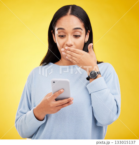 Shock, surprise and woman in studio with phone and hand on mouth isolated on yellow background. Social media, fake news or exciting online promotion, hispanic girl reading notification on smartphone. Shock, surprise and woman in studio with phone and hand on mouth isolated on yellow background. Social media, fake news or exciting online promotion, hispanic girl reading notification on smartphone. 133015137