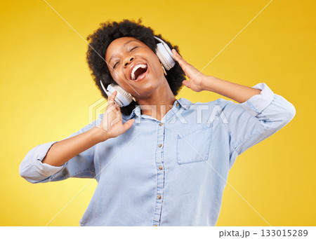 Black woman, headphones and freedom, listening to music and happiness with dance on yellow studio background. Happy female, carefree and sing along to radio, audio streaming with fun and technology 133015289