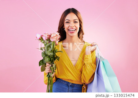 Happy, shopping bags and flowers with portrait of woman in studio for retail, birthday and spring. Event, party and smile with female and roses on pink background for sale, discount and romance 133015474