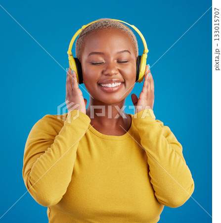 Black woman, face and headphones, listening to music with rhythm and fun with freedom on blue background. Happy female with smile, streaming radio or podcast with peace and eyes closed in studio 133015707