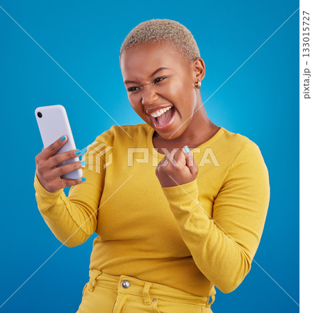 Black woman, phone and fist celebration in studio, blue background and winning online prize. Happy female model celebrate mobile promotion, bonus and excited for deal, success and competition winner 133015727