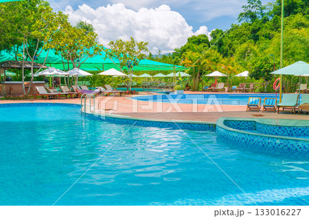 sun umbrellas and beds by swimming pool at luxury resort in nature in summer. Landscape with outdoor pool with blue water in spa hotel. Vacation and relaxation. Destination for tourism sun umbrellas and beds by swimming pool at luxury resort in nature in summer. Landscape with outdoor pool with blue water in spa hotel. Vacation and relaxation. Destination for tourism 133016227
