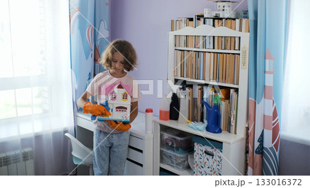 Neat girl in gloves wipes toy house with rag in bright colorful bedroom 133016372