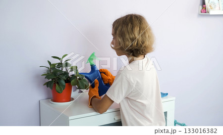 Teen girl waters houseplant with care in a cozy home interior 133016382