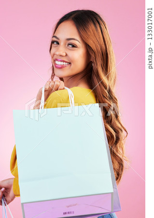Portrait, shopping and fashion with a black woman customer in studio on a pink background for retail. Face, smile or sale and an attractive young female shopper happy with a deal or promotion 133017001
