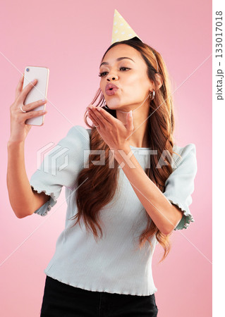 Selfie, birthday party and kiss of woman in studio isolated on a pink background. Air kissing, profile picture and mixed race female taking photo for happy memory, social media or special celebration 133017018