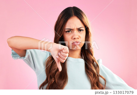 Upset, thumbs down and portrait of a female in a studio with a sad, moody or disappointed face. Loser, unhappy and young woman model posing with a angry hand gesture isolated by a pink background. 133017079