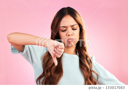 Unhappy, thumb down and sad woman in a studio with an upset, moody or disappointed face. Loser, rejection and young female model posing with a disagreement hand gesture isolated by a pink background. 133017083