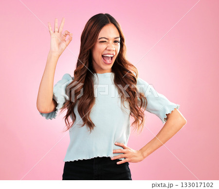 Wink, studio and female with a perfect hand gesture, excitement and positive face expression. Happy, smile and young woman model from Colombia with a ok sign language isolated by a pink background. 133017102