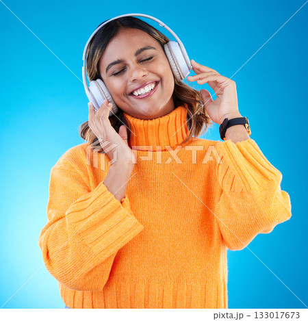 Music headphones, smile and woman in studio isolated on a blue background. Podcast, radio and happy Indian female with eyes closed streaming, listening and enjoying sound, audio or song with headset. 133017673