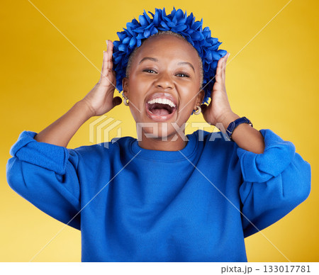 Portrait, queen and flower crown with an excited black woman in studio on a yellow background. Face, expression and sustainability with an attractive female wearing a blue wreath as royalty 133017781