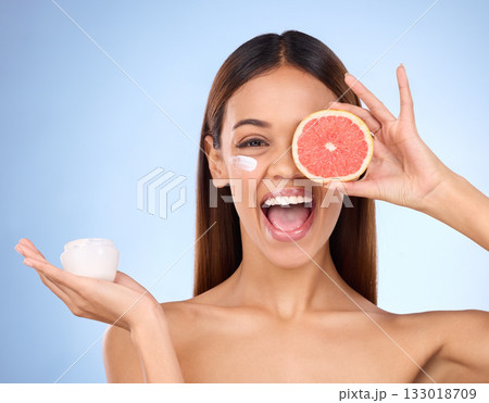 Woman, moisturizer cream and grapefruit for natural skincare beauty and vitamin C against blue studio background. Portrait of happy female holding fruit, creme or lotion for healthy organic products 133018709