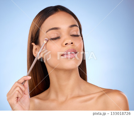 Eyeshadow brush, woman and makeup for eyes with cosmetics on face in studio. Aesthetic female model person on a blue background for self care, facial glow and powder with skin shine for beauty 133018726