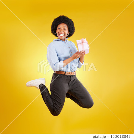Jump, excited and black woman with gift in air on yellow background with energy, happy and smile in studio. Birthday mockup, celebrate and isolated girl jumping with present, box and surprise package 133018845