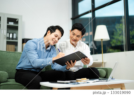 Two Asian businessmen smiling while signing a contract on clipboard, symbolizing business cooperation, teamwork Two Asian businessmen smiling while signing a contract on clipboard, symbolizing business cooperation, teamwork 133019090
