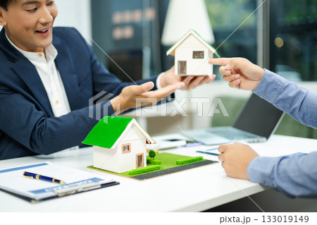 Real estate agent consulting with buyer on house model and pricing using calculator in modern office. and client service. 133019149