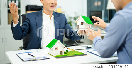 Real estate agent consulting with buyer on house model and pricing using calculator in modern office. and client service. Real estate agent consulting with buyer on house model and pricing using calculator in modern office. and client service. 133019150