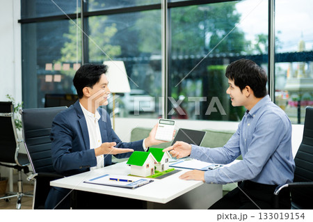 Real estate agent consulting with buyer on house model and pricing using calculator in modern office. and client service. 133019154