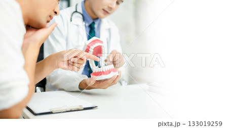 Dentist explaining dental health to male patient using model jaw. Oral care, tooth pain consultation, anatomy education 133019259