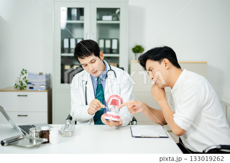 Dentist explaining dental care to male patient using a tooth model. Health consultation, oral hygiene, and professional support 133019262