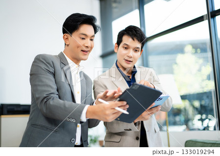Two Asian businessmen using tablet and smartphone for project planning in a modern office. Two Asian businessmen using tablet and smartphone for project planning in a modern office. 133019294