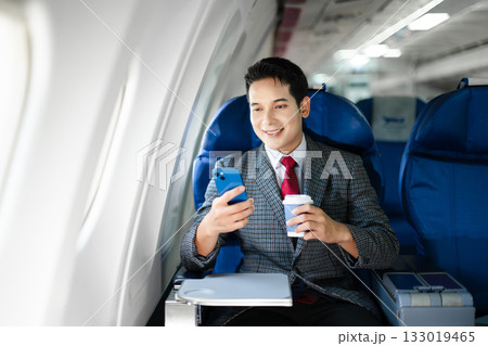 Confident businessman in first class holding coffee and using his smartphone, showcasing luxury air travel, success, and a modern professional lifestyle. Confident businessman in first class holding coffee and using his smartphone, showcasing luxury air travel, success, and a modern professional lifestyle. 133019465