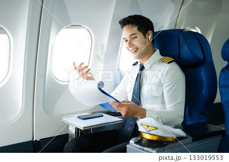 Asian Confident male pilot in uniform leaning at the passenger seat while standing inside of the airplane flight cockpit during takeoff and checking flight plan Asian Confident male pilot in uniform leaning at the passenger seat while standing inside of the airplane flight cockpit during takeoff and checking flight plan 133019553