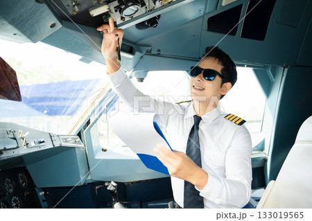 Professional airline pilot in uniform inspecting cockpit control panels during safety checks, ideal for aviation, travel, and airline safety themes. Professional airline pilot in uniform inspecting cockpit control panels during safety checks, ideal for aviation, travel, and airline safety themes. 133019565