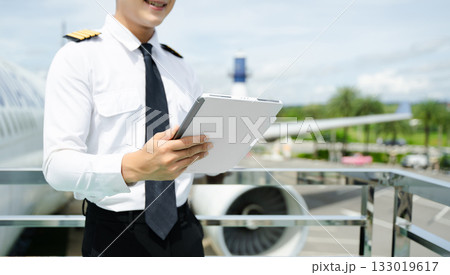 Airline pilot in uniform reviewing checklist outdoors by airplane, perfect for aviation, travel, and professional flight safety themes Airline pilot in uniform reviewing checklist outdoors by airplane, perfect for aviation, travel, and professional flight safety themes 133019617