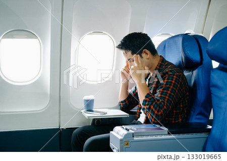 Travel stress, jet lag, or motion sickness. Young man with a headache or fatigue during a long flight. Tired passenger on a business trip. Travel stress, jet lag, or motion sickness. Young man with a headache or fatigue during a long flight. Tired passenger on a business trip. 133019665