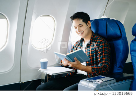 Happy young man traveling by plane. Business or leisure flight series showing phone talk, tech, reading, and stress. 133019669