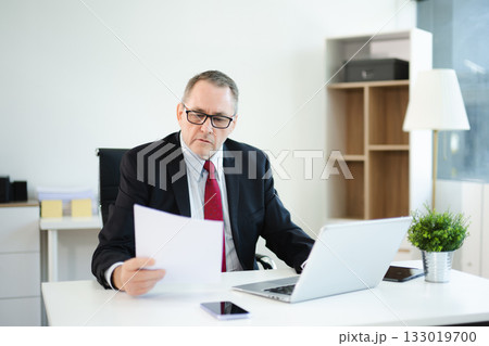 Confident businessman in suit, working on laptop and smartphone at office desk. Professional executive, leadership, strategy 133019700