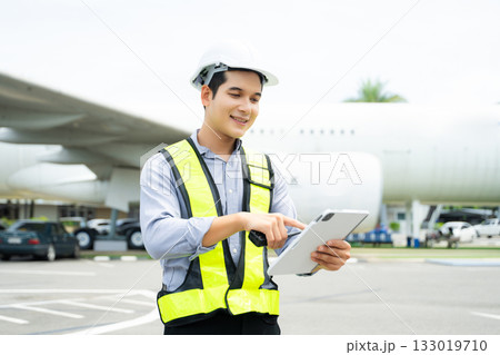 Ground crew engineer in safety vest and hard hat using walkie talkie while checking documents, perfect for aviation, maintenance, Ground crew engineer in safety vest and hard hat using walkie talkie while checking documents, perfect for aviation, maintenance, 133019710