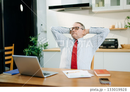 Mature Businessman using laptop while sitting at home. man sitting in kitchen Mature Businessman using laptop while sitting at home. man sitting in kitchen 133019928